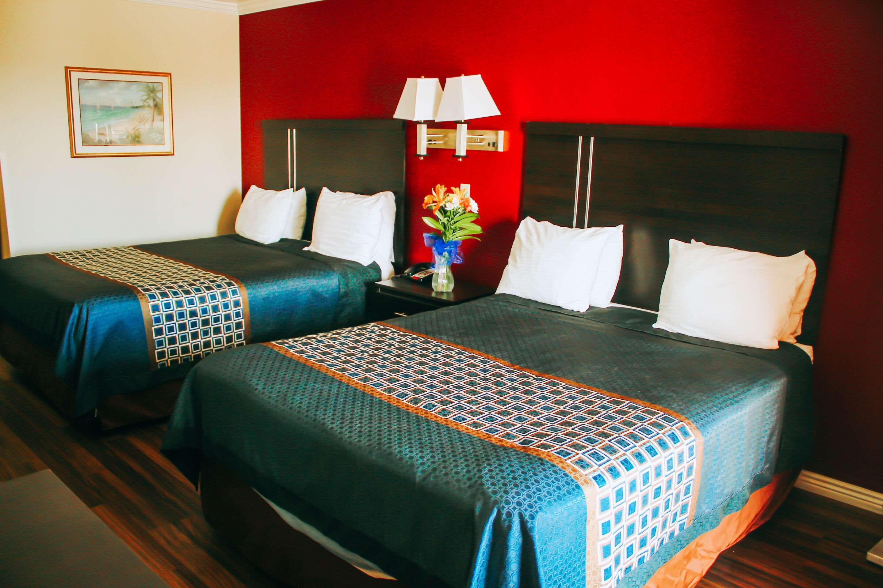 A hotel room with two beds, each with a patterned bedspread, a nightstand with a lamp, and a vase with flowers.