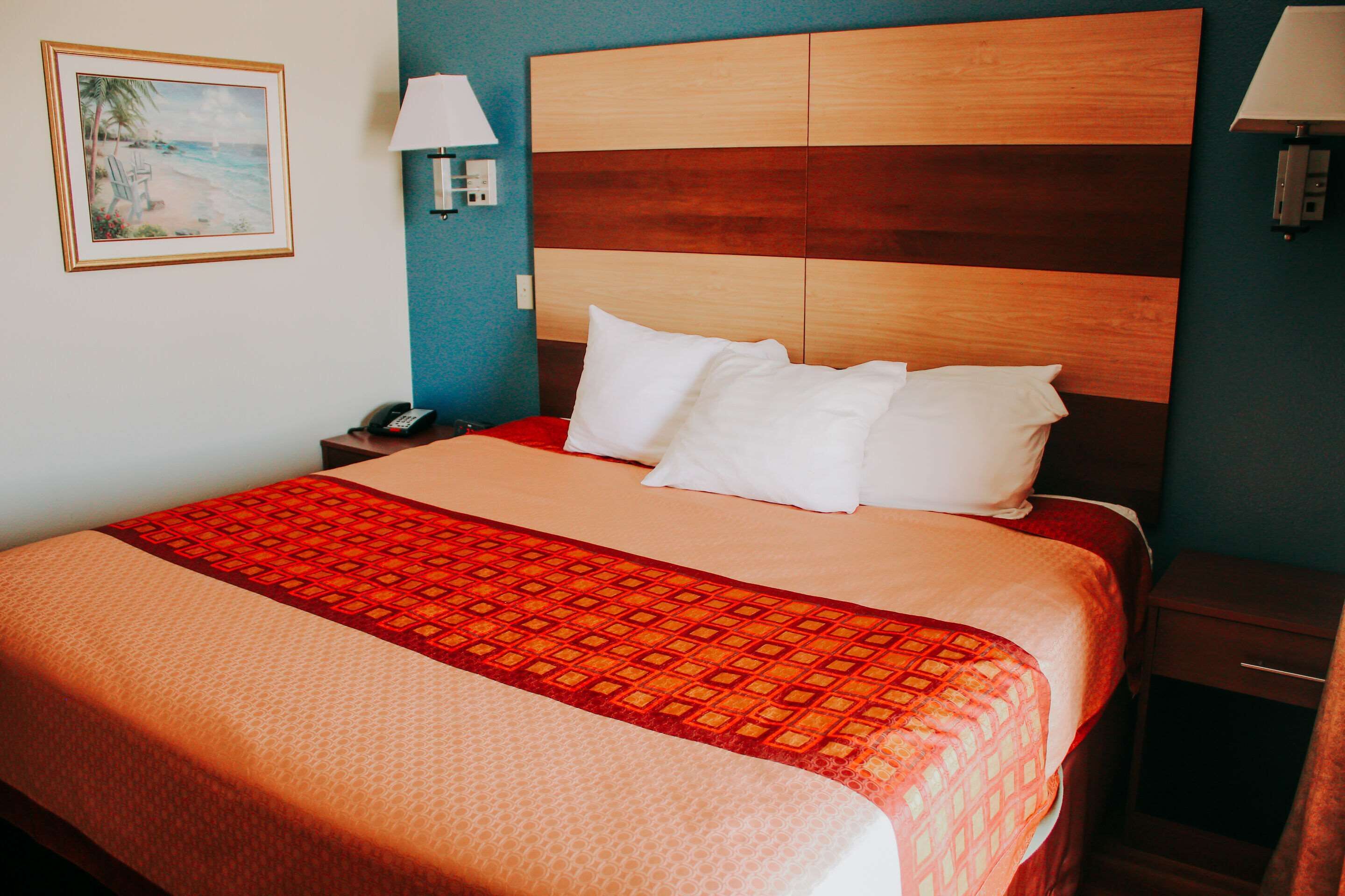A hotel room with a bed, a nightstand, a lamp, and a painting on the wall.
