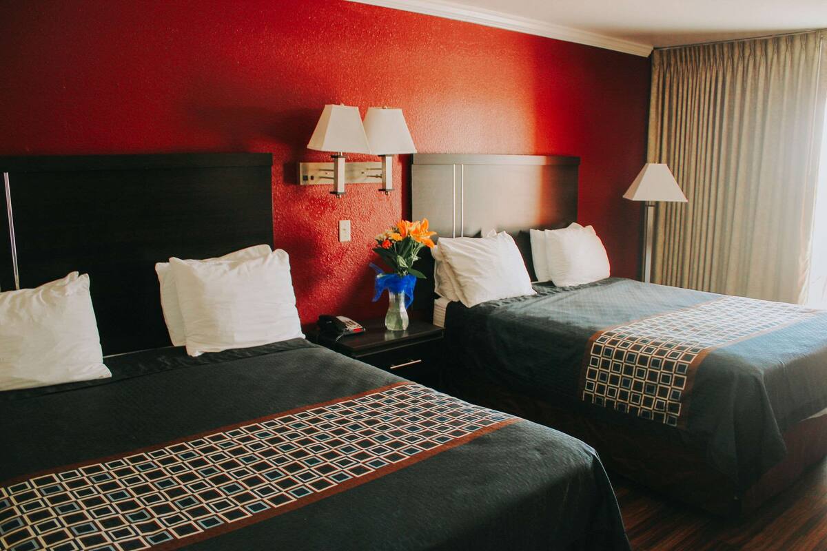 Ein Hotelzimmer mit zwei Betten, einem Nachttisch, einer Vase mit Blumen und einer roten Wand.