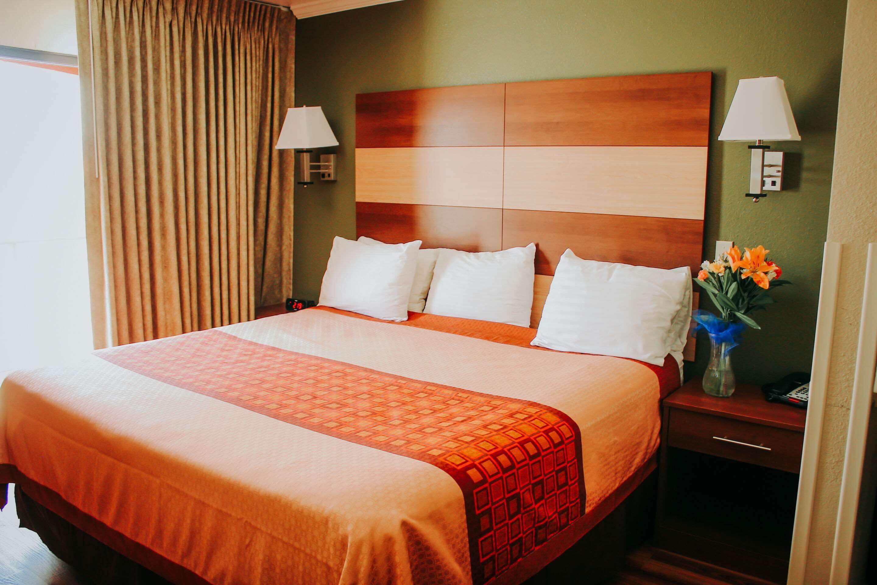 A hotel room with a large bed, two bedside lamps, a nightstand with a vase of flowers, and a wooden headboard.
