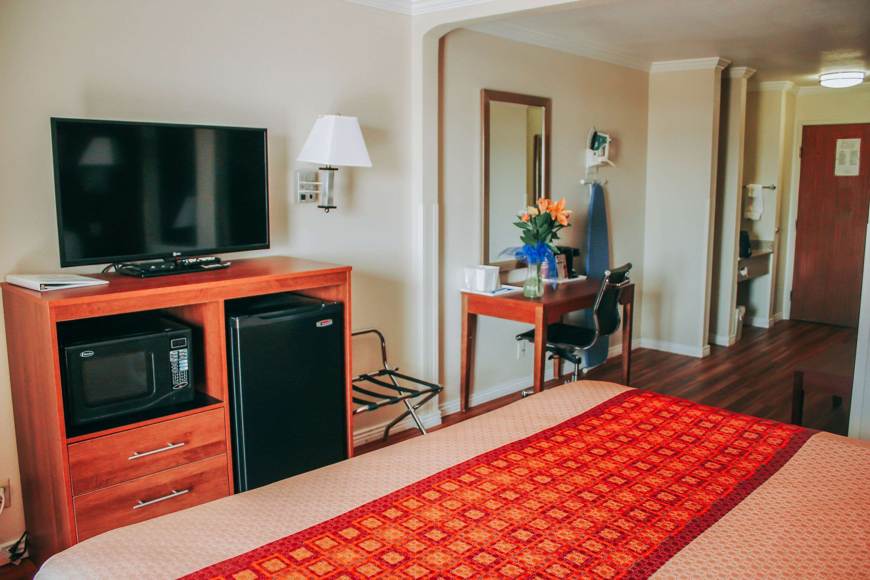 Une chambre d’hôtel équipée d’un lit, d’une télévision, d’un four à micro-ondes, d’un réfrigérateur, d’un bureau avec une chaise et d’un miroir.