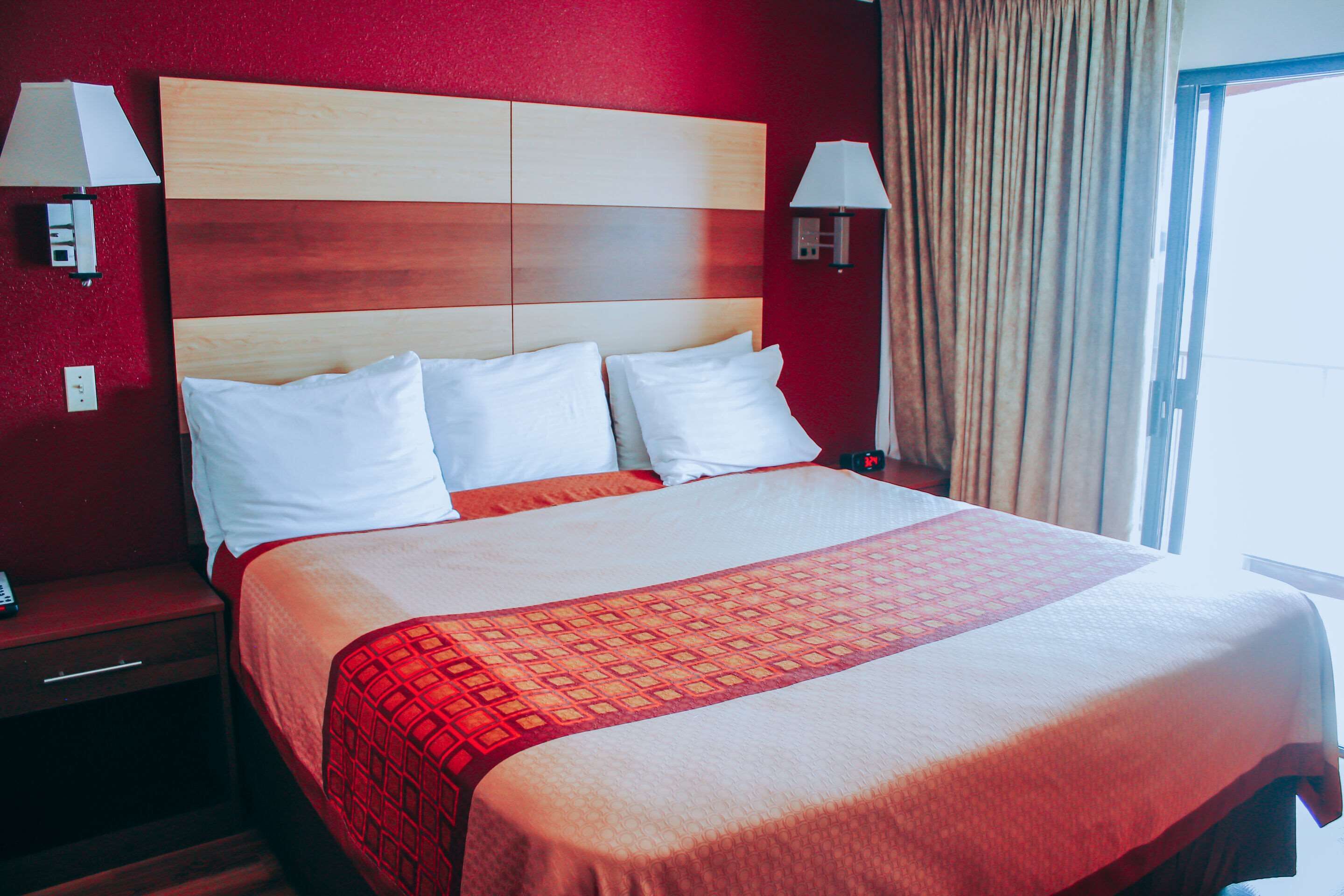 A hotel room with a large bed, two bedside lamps, and a window with curtains.