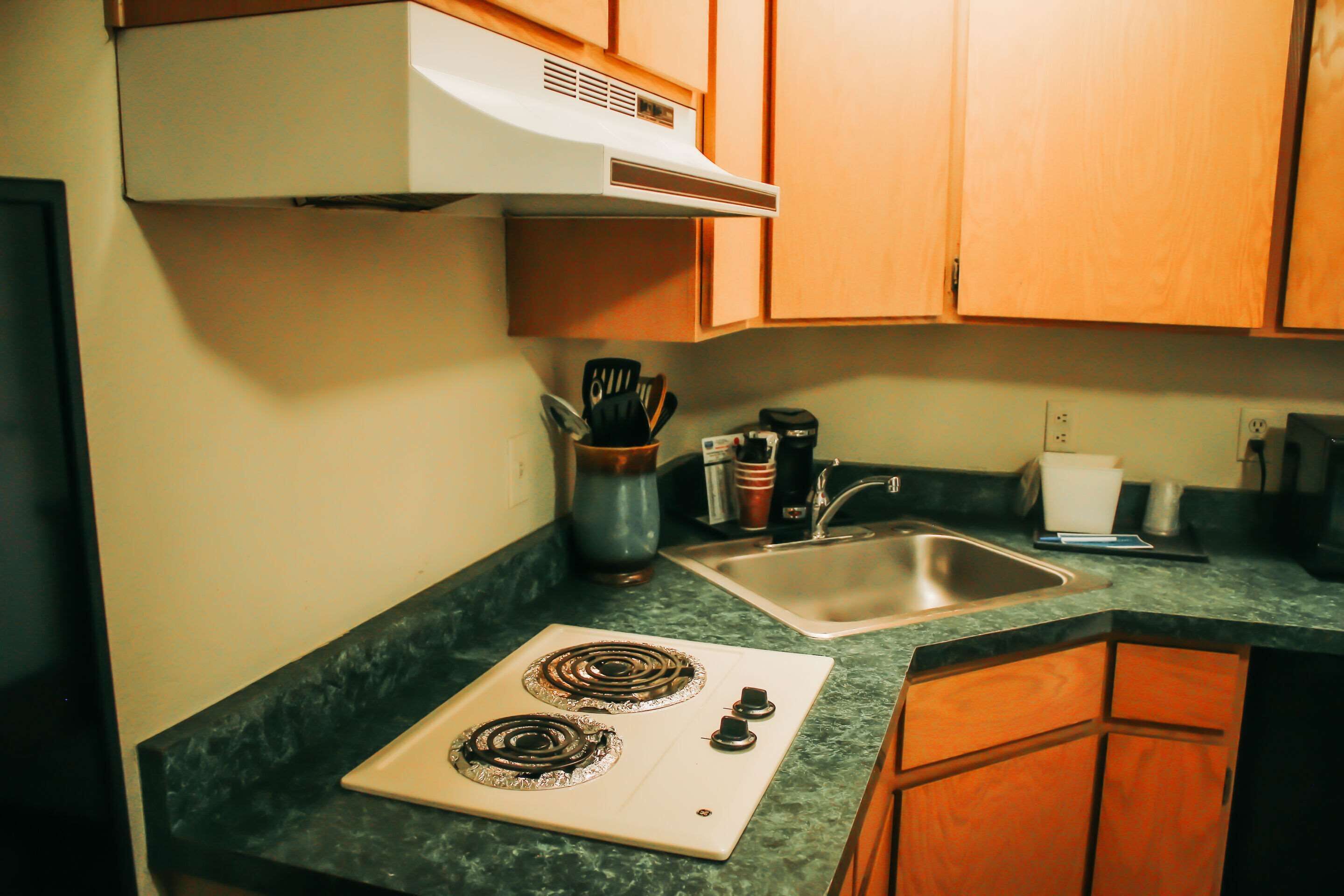 A kitchen with a stove, sink, and wooden cabinets.