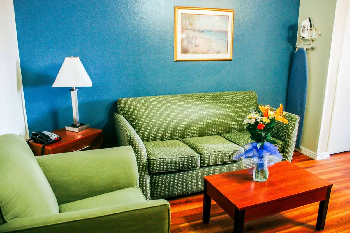 Ein Zimmer mit einem grünen Sofa, einem Holztisch mit Blumenvase, einer Lampe und einem Bild an der Wand.