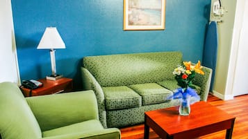 Una habitación con un sofá verde, una mesa de centro de madera con un jarrón de flores, una lámpara y un cuadro en la pared.