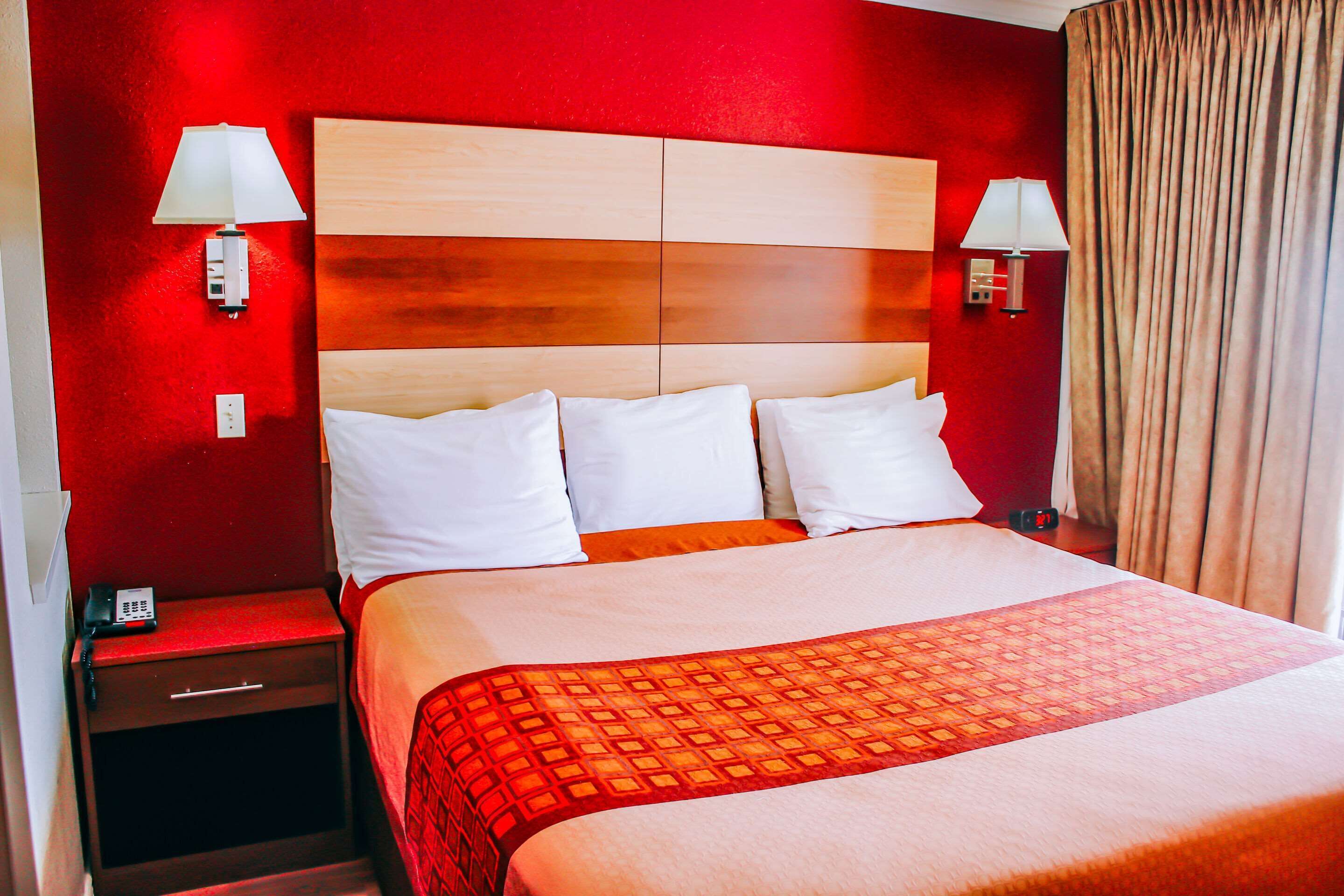 A hotel room with a red wall, a wooden headboard, white bedding, and two bedside lamps.