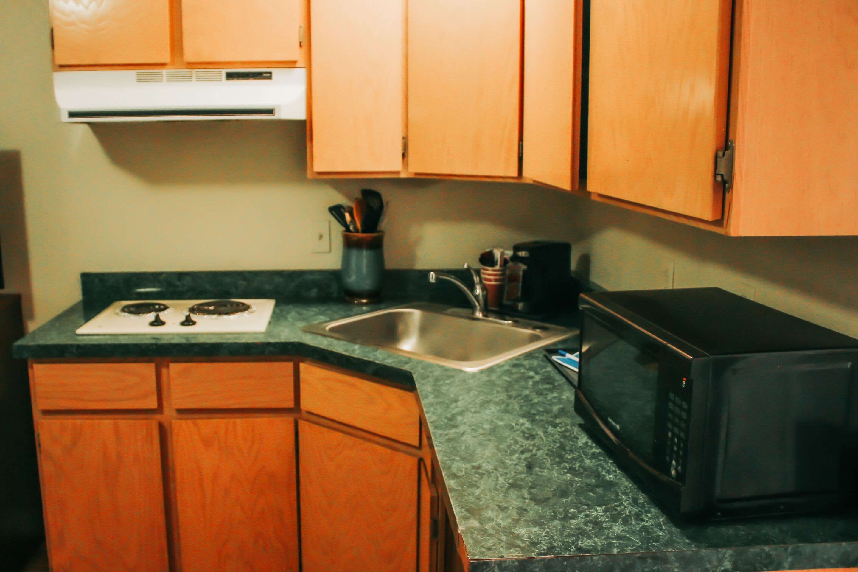 Una cocina con armarios de madera, un lavamanos de acero inoxidable, una estufa y un microondas.