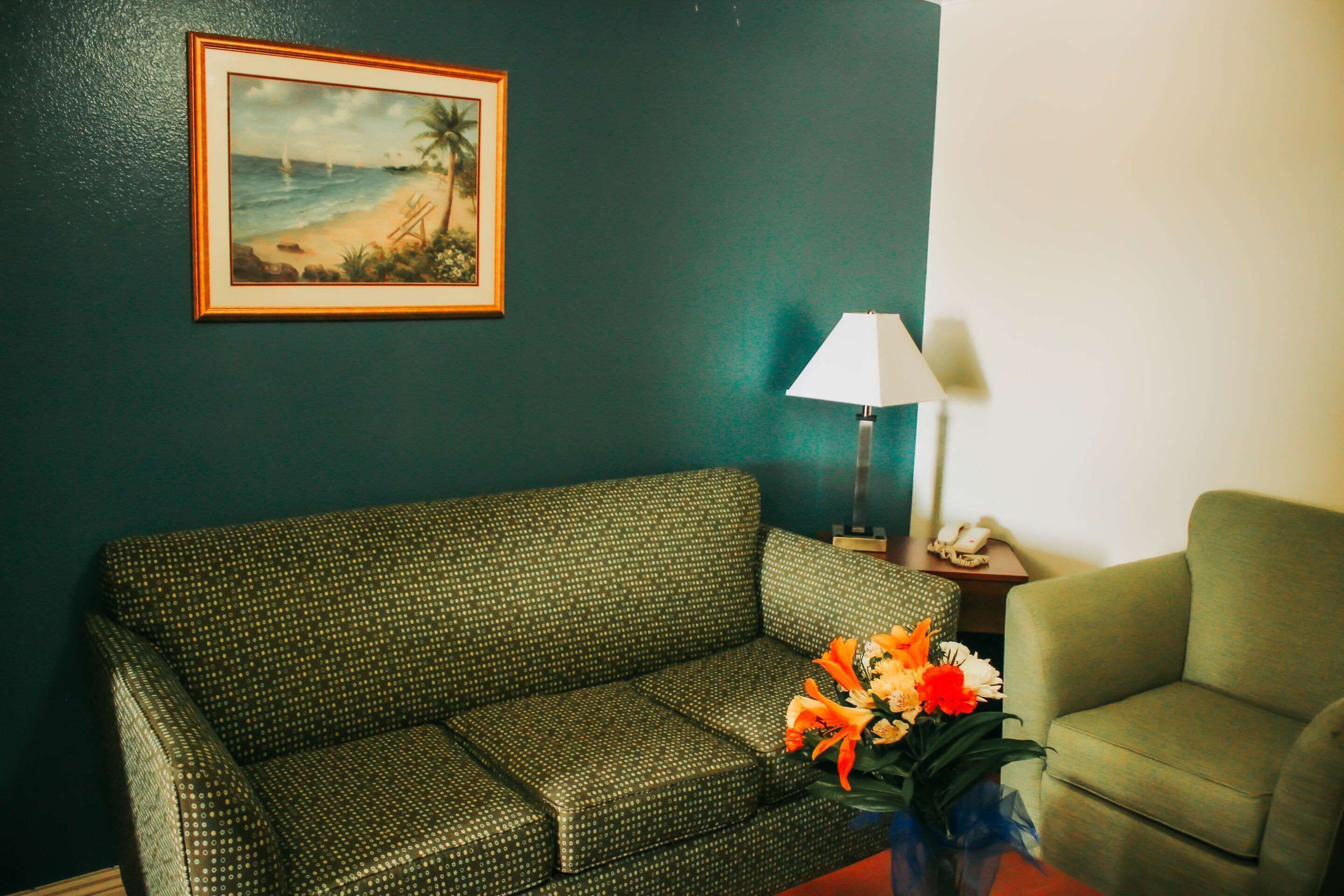 A room with a green sofa, a small table with a lamp, and a framed picture on the wall.