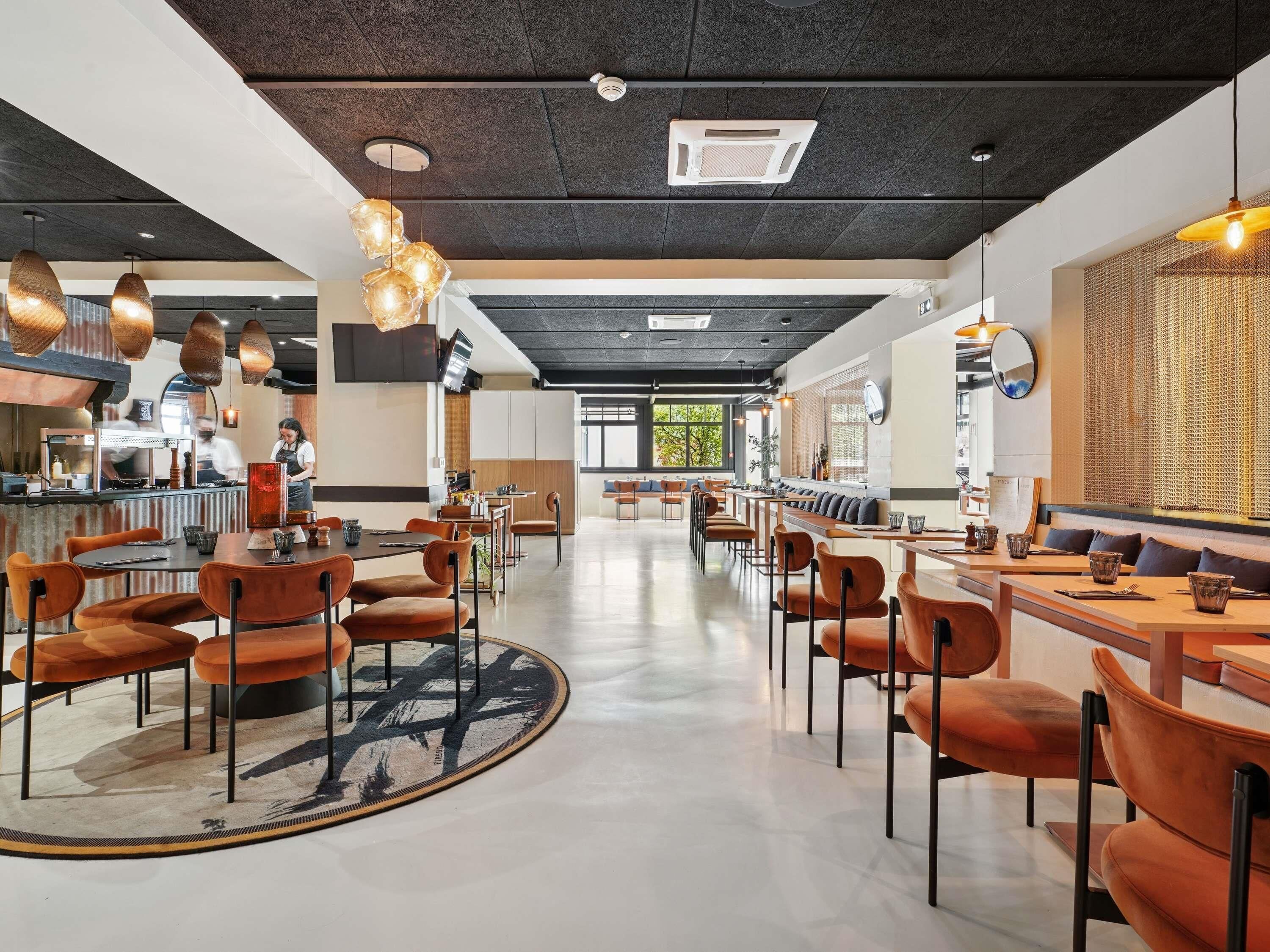 A modern restaurant interior with high tables, orange chairs, and pendant lighting.