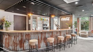A bar area with a wooden counter, bar stools, and a Coca-Cola sign. - ibis Paris Porte d'Orléans (Montrouge)