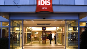 A hotel entrance with a glass facade, a digital display, and a reception area. - ibis Paris Porte d'Orléans (Montrouge)