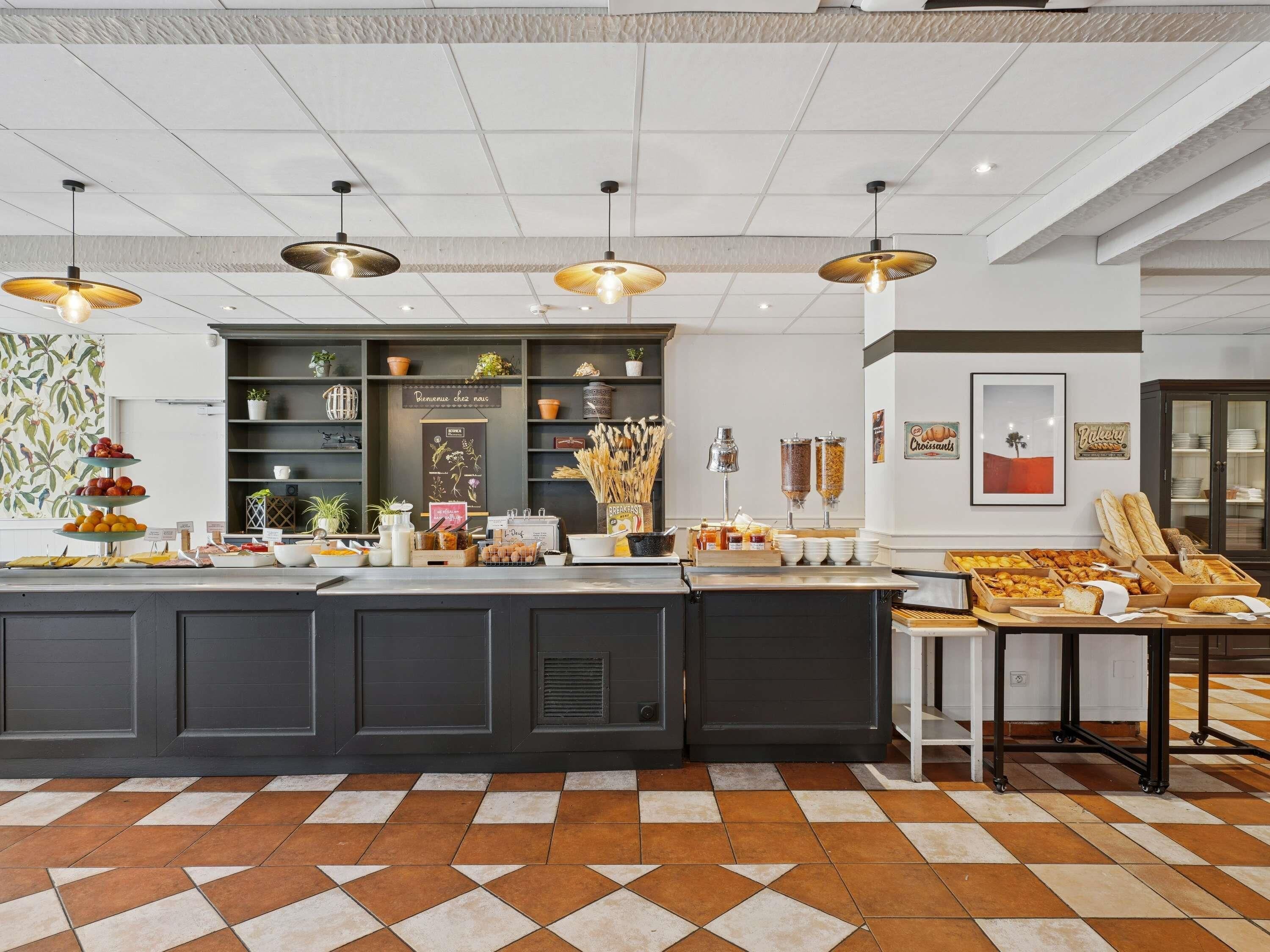 Un café moderne avec un comptoir central, des étagères remplies de produits de boulangerie et un sol carrelé.
