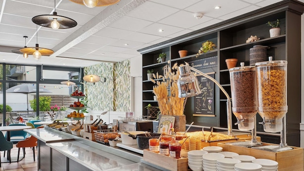 A breakfast buffet with various food items, a coffee station, and a seating area with tables and chairs. - ibis Paris Porte d'Orléans (Montrouge)