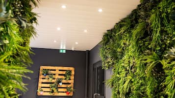 Una habitación con una pared oscura, una decoración vegetal en una pared de palets de madera, y una puerta con pomo.