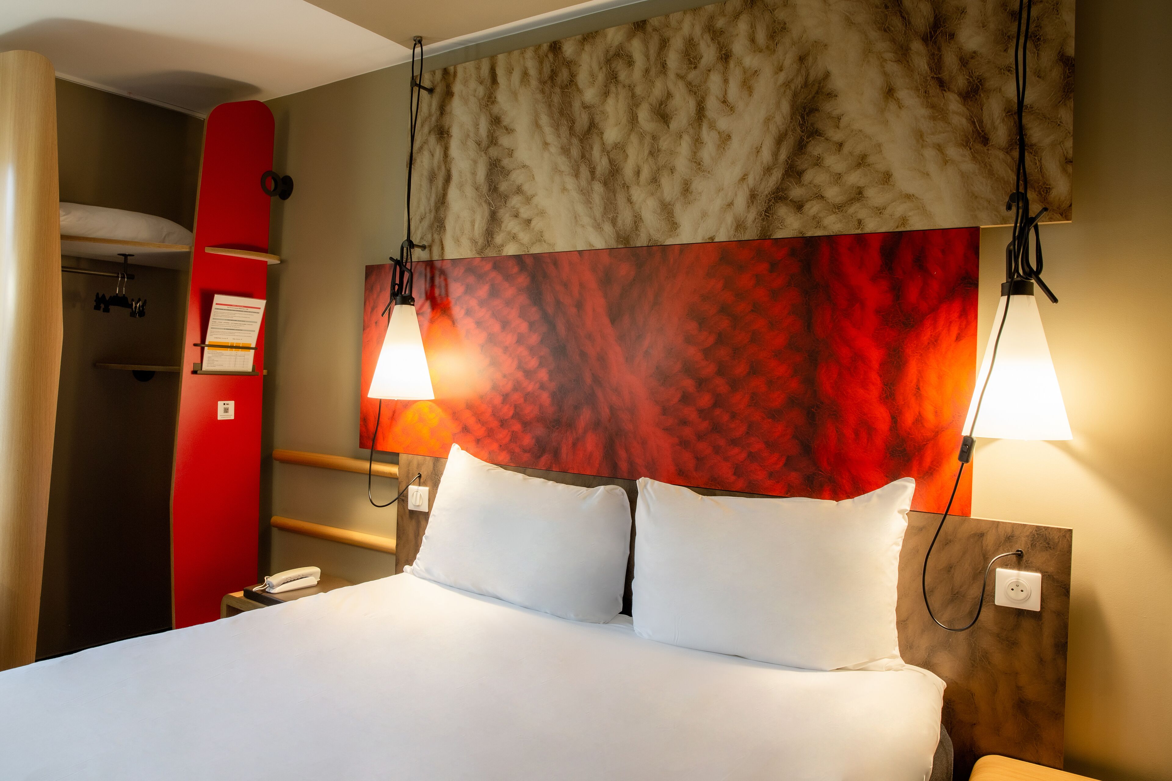 Habitación de hotel con cama, dos lámparas de noche, pared roja y cabecera de madera.