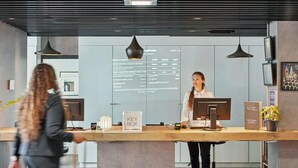 A modern reception desk with a digital display, a key box, and a sign for "All Guests Welcome." - ibis Paris Porte d'Orléans (Montrouge)