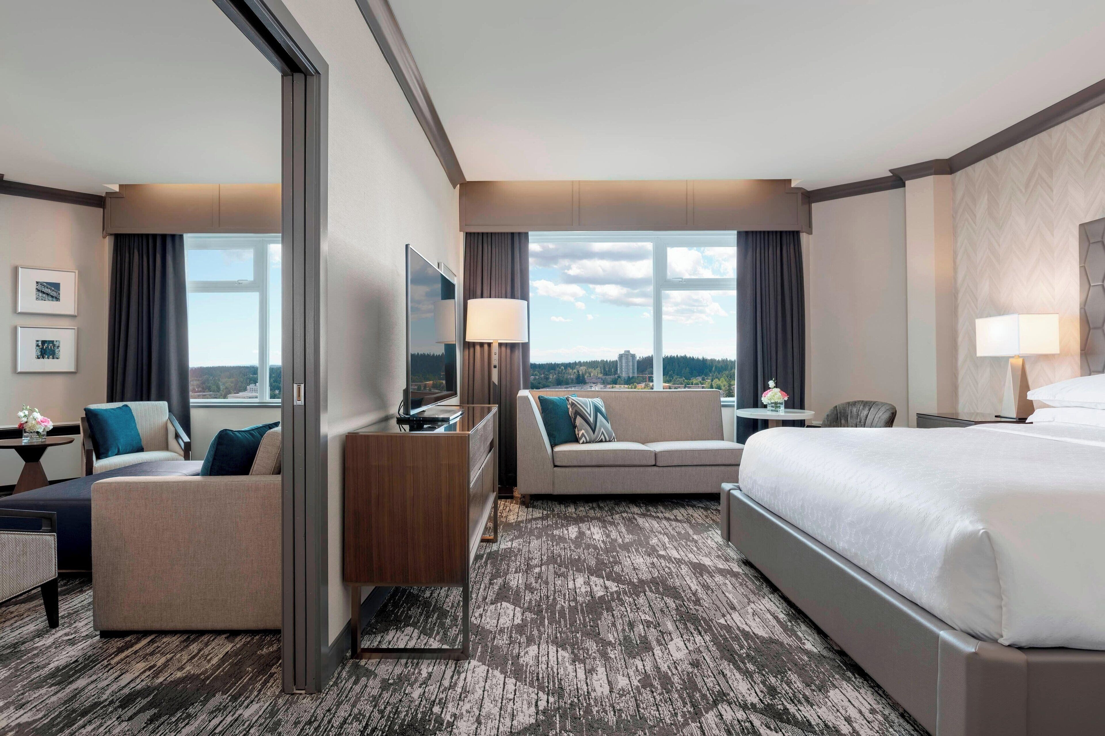 Een hotelkamer met een bed, een bank, een bureau, een televisie en uitzicht op de stad.