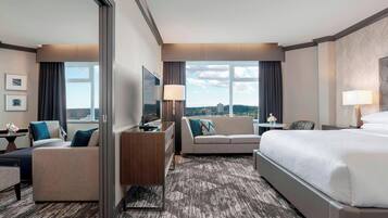 Een hotelkamer met een bed, een bank, een bureau, een televisie en uitzicht op de stad.