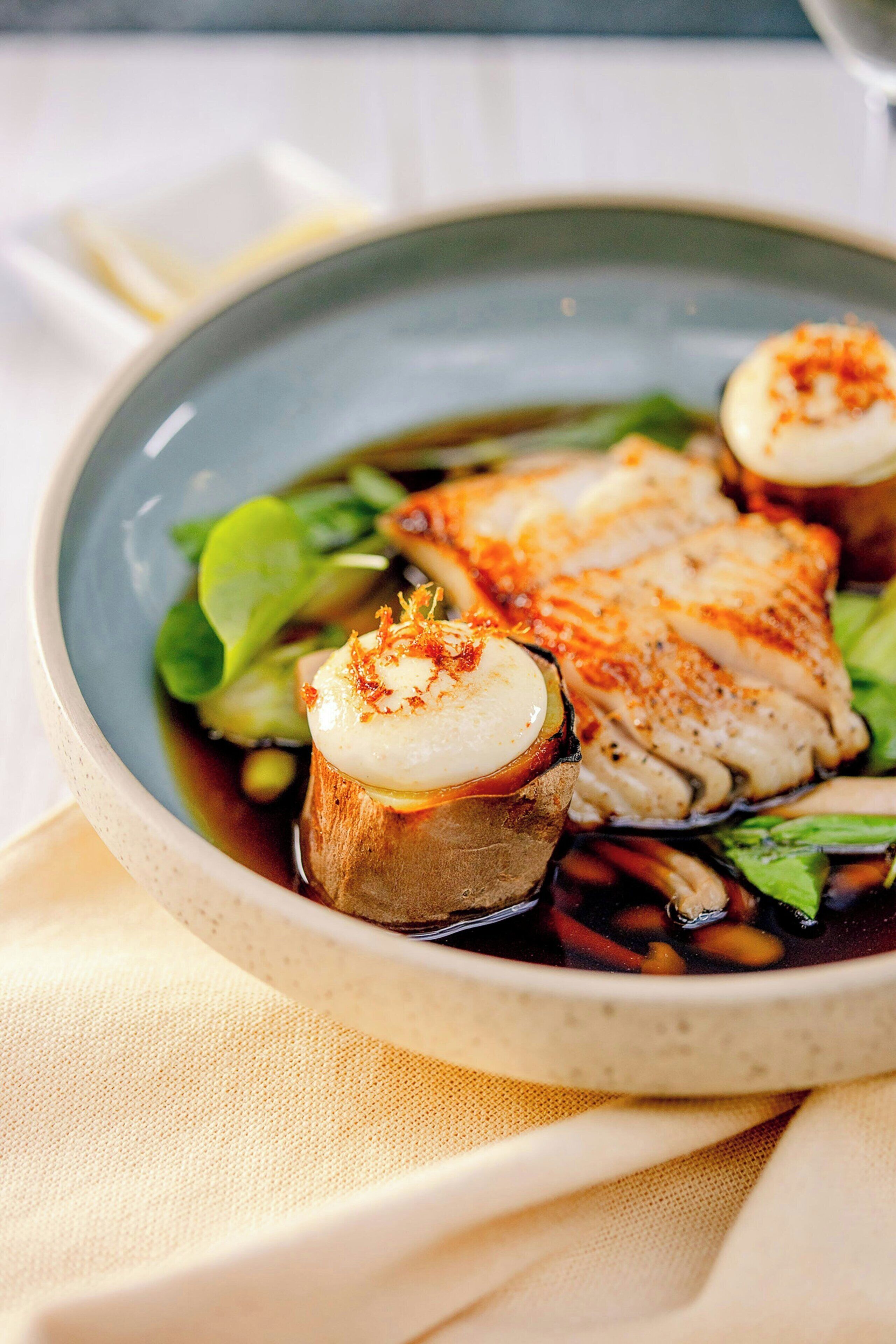 Un plato de comida con filete de pescado, hongos y vegetales verdes.