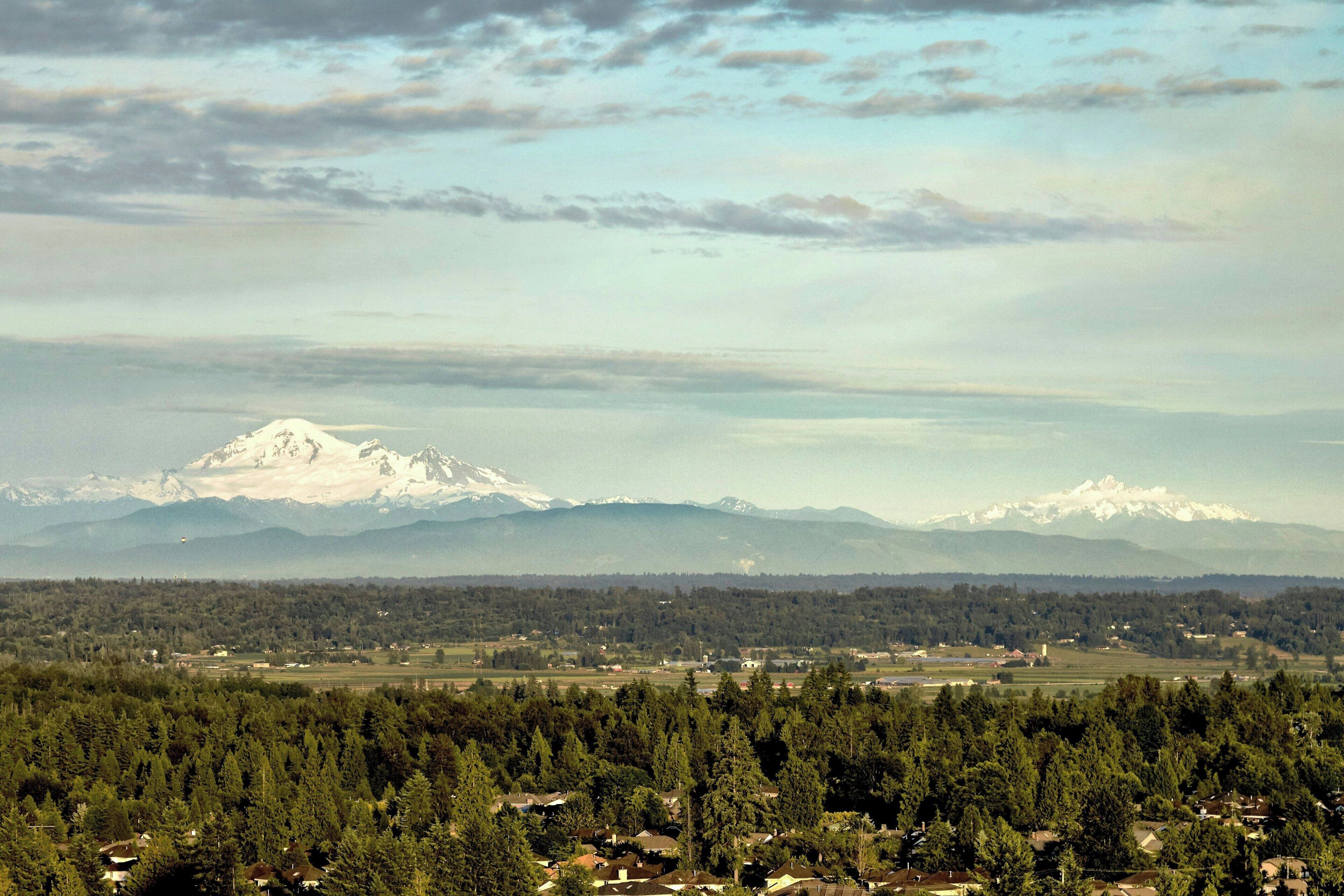 A mountainous landscape with snow-capped peaks and a forested valley below.