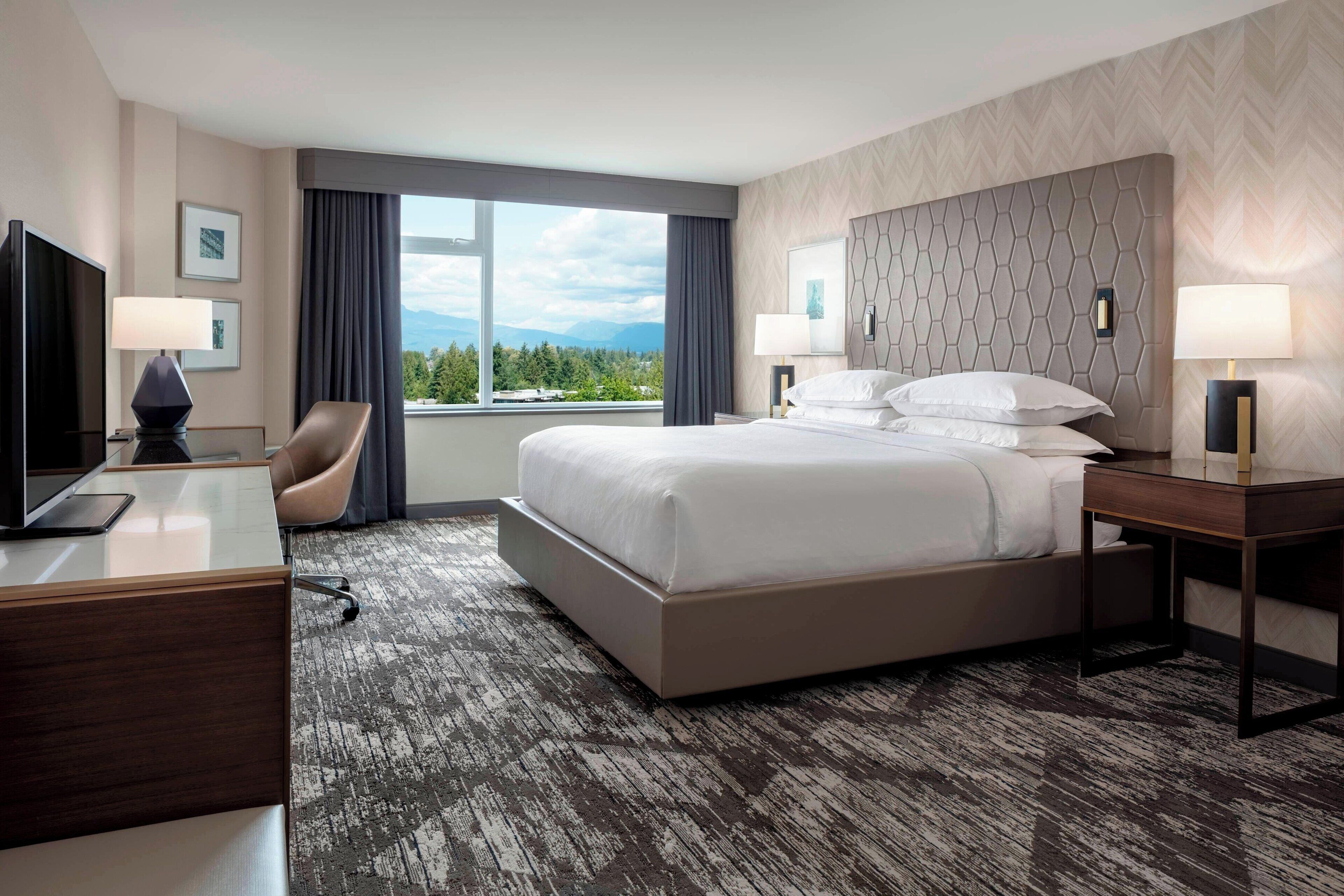 A hotel room with a large bed, a desk with a computer, a chair, and a TV.