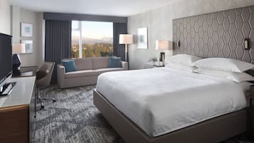 Quarto de hotel com uma cama grande, um sofá, uma escrivaninha e vista para as montanhas.