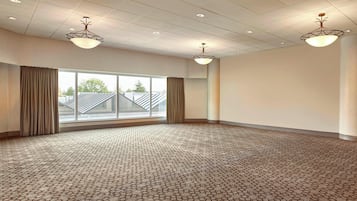 A spacious room with a patterned carpet, large windows with curtains, and ceiling lights.