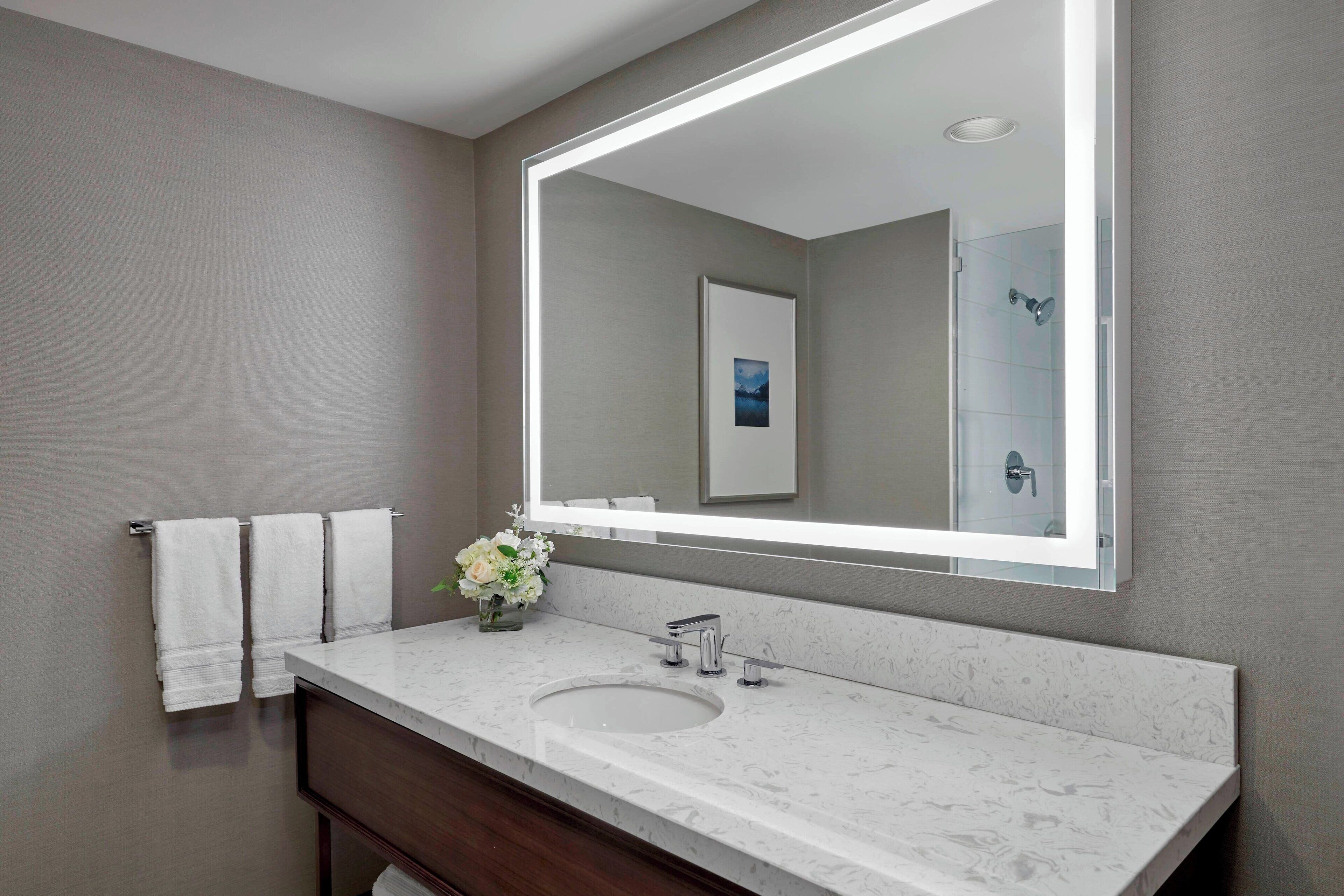 A modern bathroom with a large mirror, a marble sink, and two towels hanging on the wall.