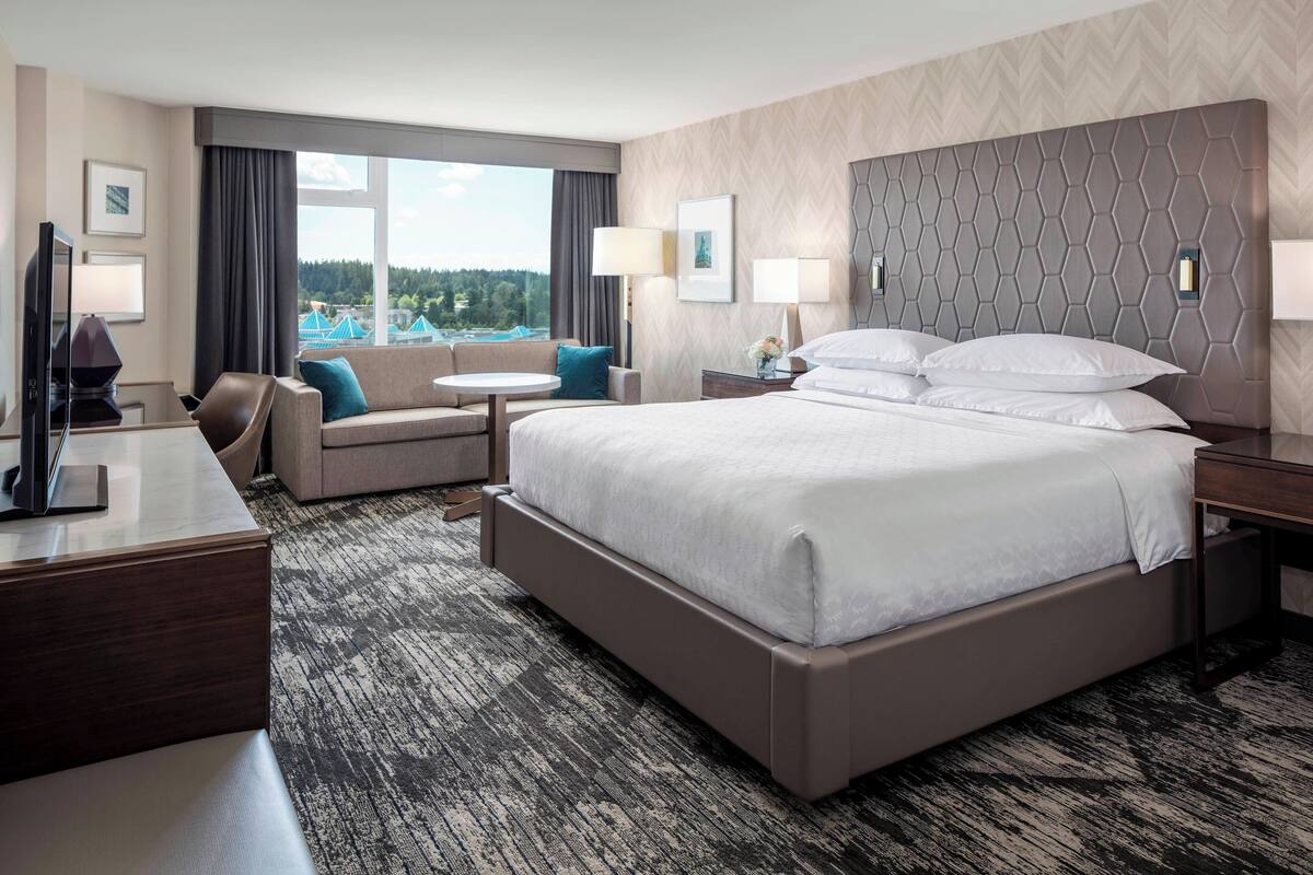 Habitación de hotel con una cama grande, un escritorio, un sofá y vistas a un paisaje urbano.