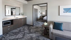 Habitación de hotel moderna con un espejo grande, armarios de madera oscura, un sofá gris y una pequeña mesa redonda con un florero.