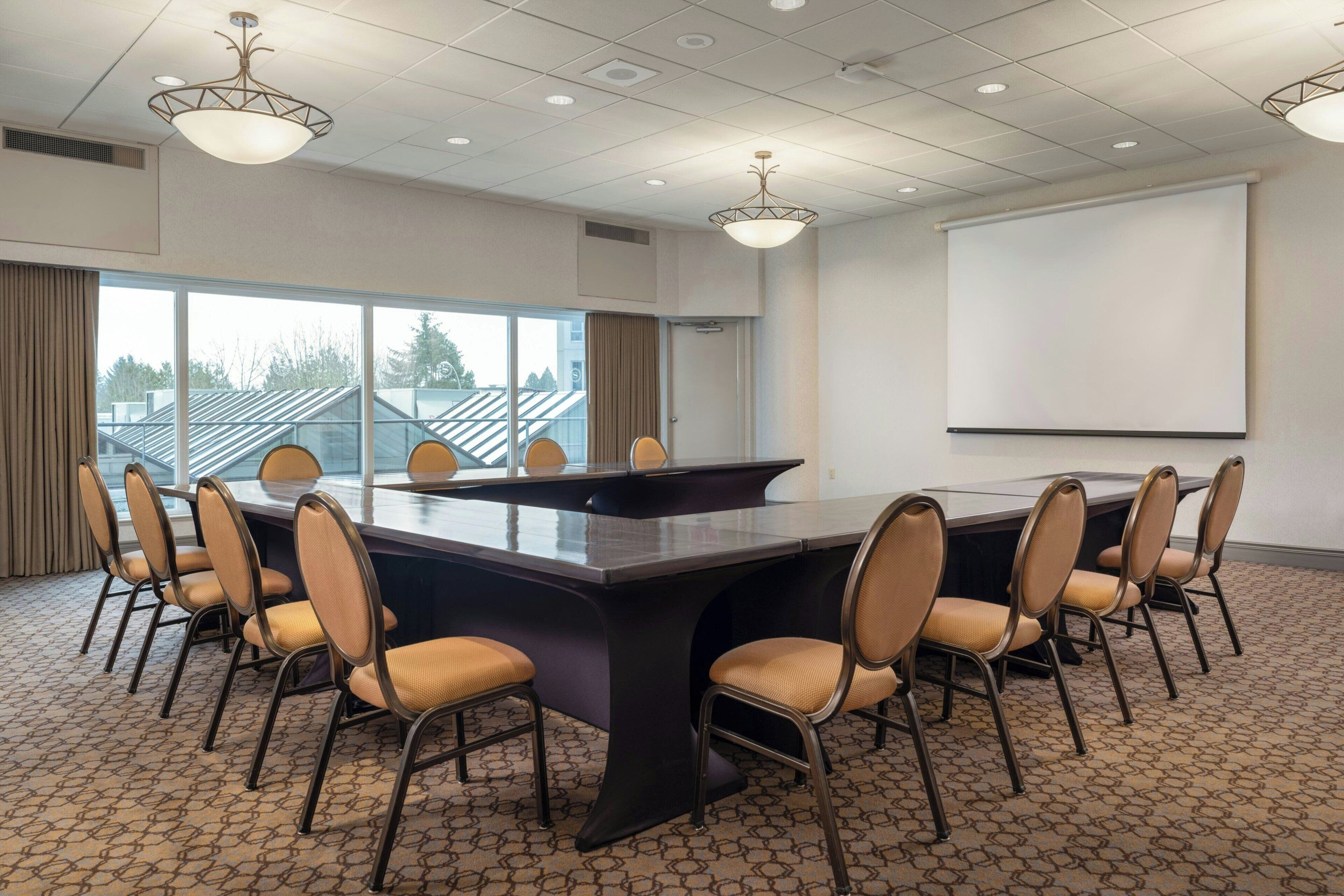 A conference room with a large table, chairs, a projector screen, and large windows.