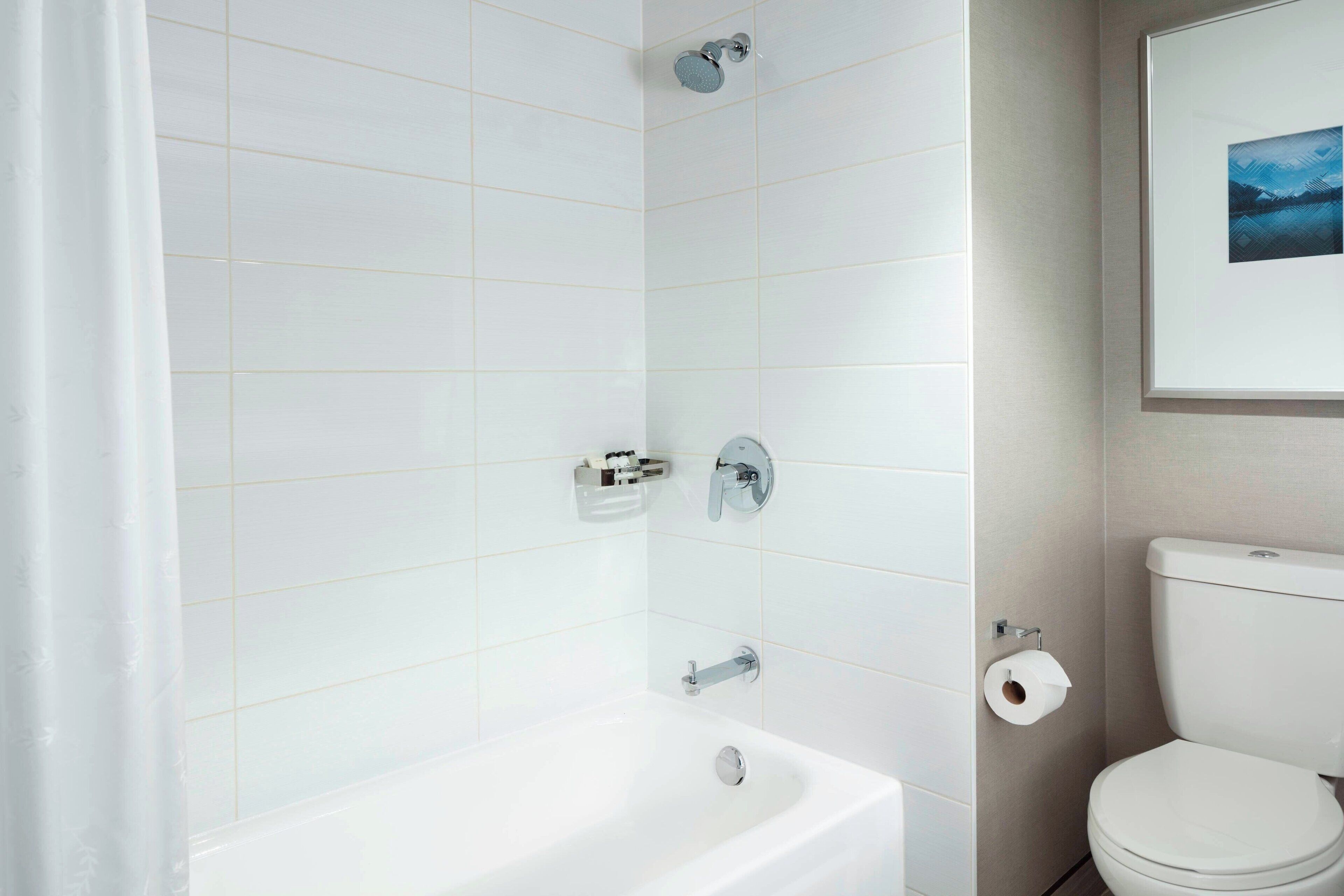 A bathroom with white tiles, a bathtub, a toilet, and a framed picture on the wall.