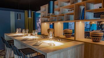 A modern bar area with a long wooden counter, multiple hanging pendant lights, and wicker baskets.