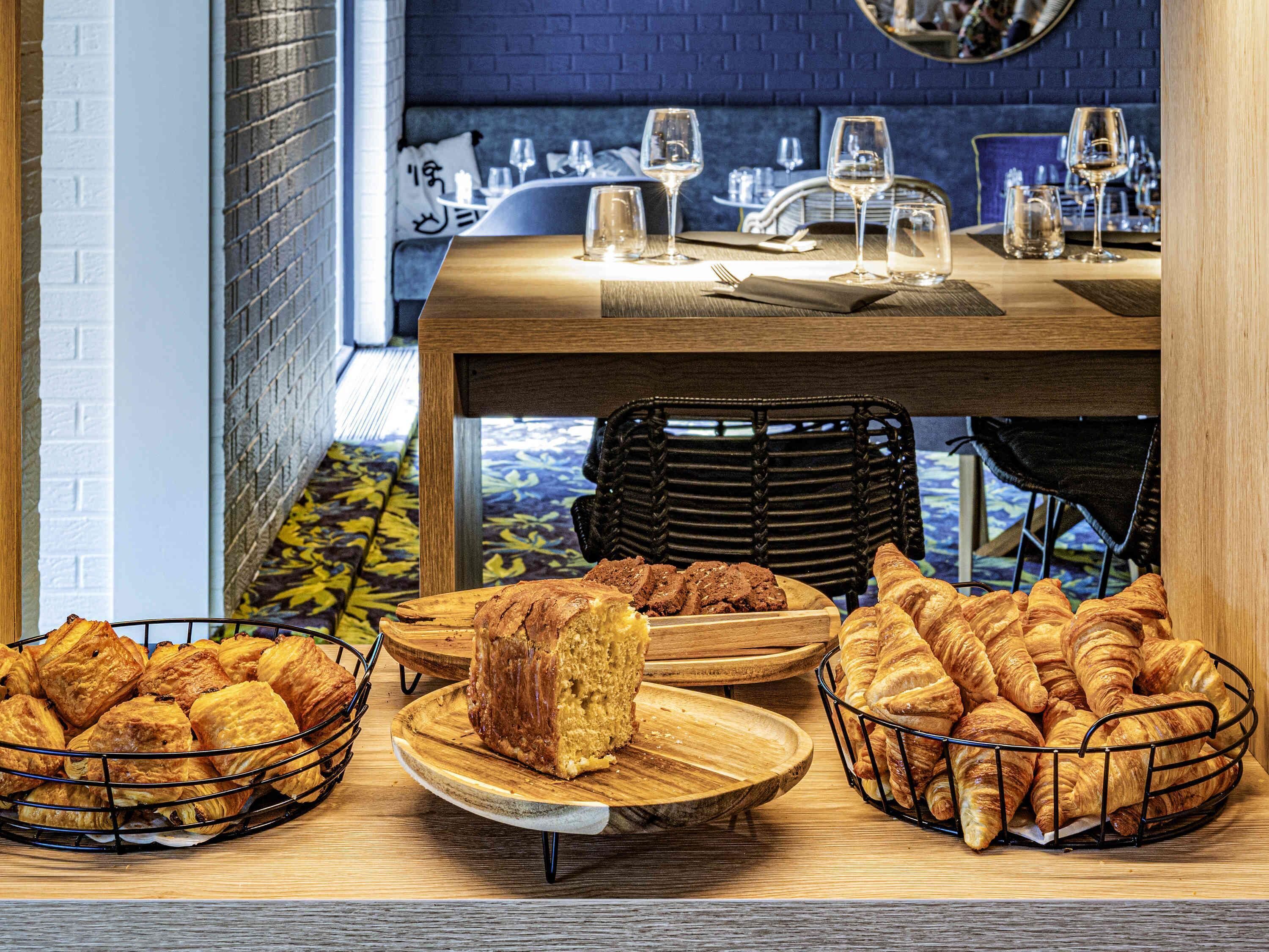 Un comedor con una mesa lista para dos personas, con pan y pastelería.