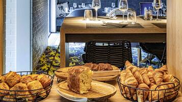 Un comedor con una mesa lista para dos personas, con pan y pastelería.