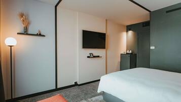 Een moderne hotelkamer met een bed, een flatscreen televisie, een nachtkastje, een lamp en een klein plankje met decoratieve objecten.