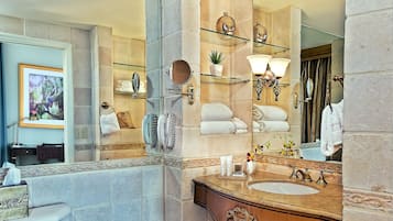 A bathroom with a large mirror, a sink with a vanity, and a toilet. There are towels and toiletries on shelves, and a framed picture on the wall.