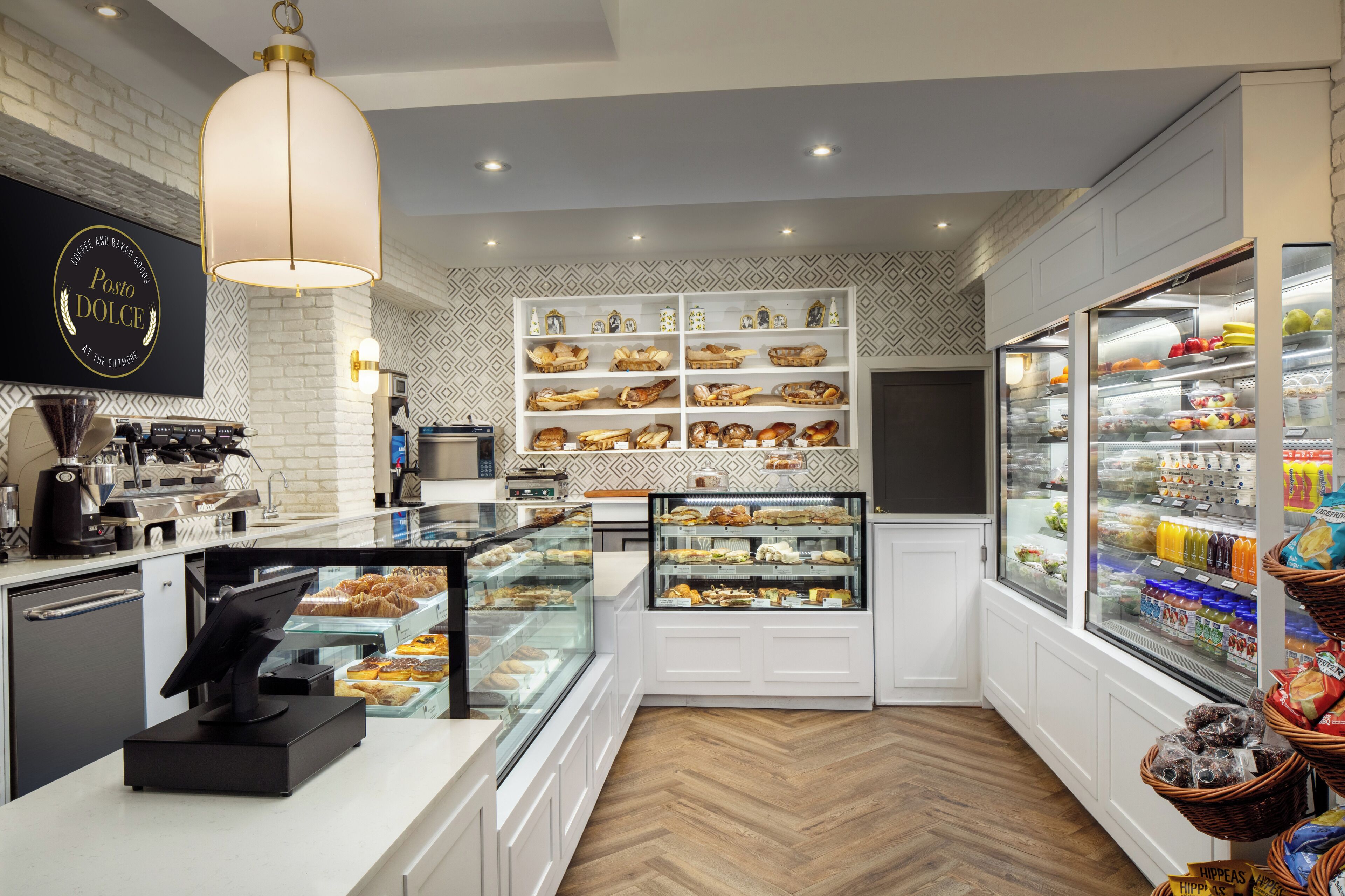 Una panadería con interior blanco, una caja registradora y estantes llenos de productos horneados.
