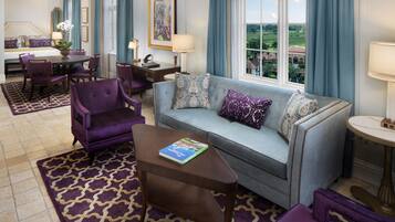 A hotel room with a sofa, purple armchairs, a dining table, and a view of the outdoors.