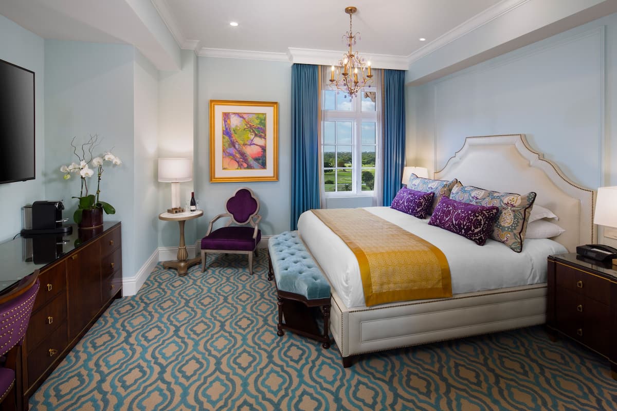 A bedroom with a large bed, a television, a desk, and a window with curtains.