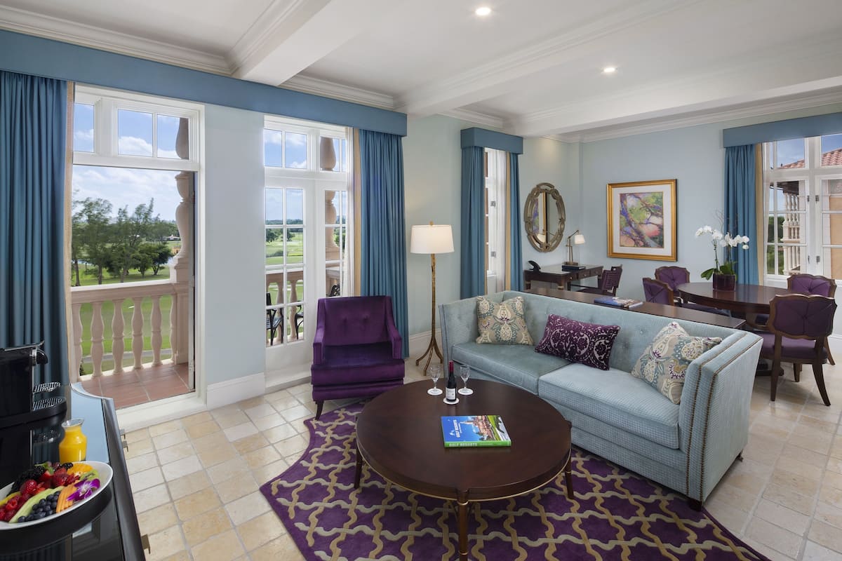 A spacious living room with a light blue sofa, a purple armchair, and a dining area with a table and chairs.