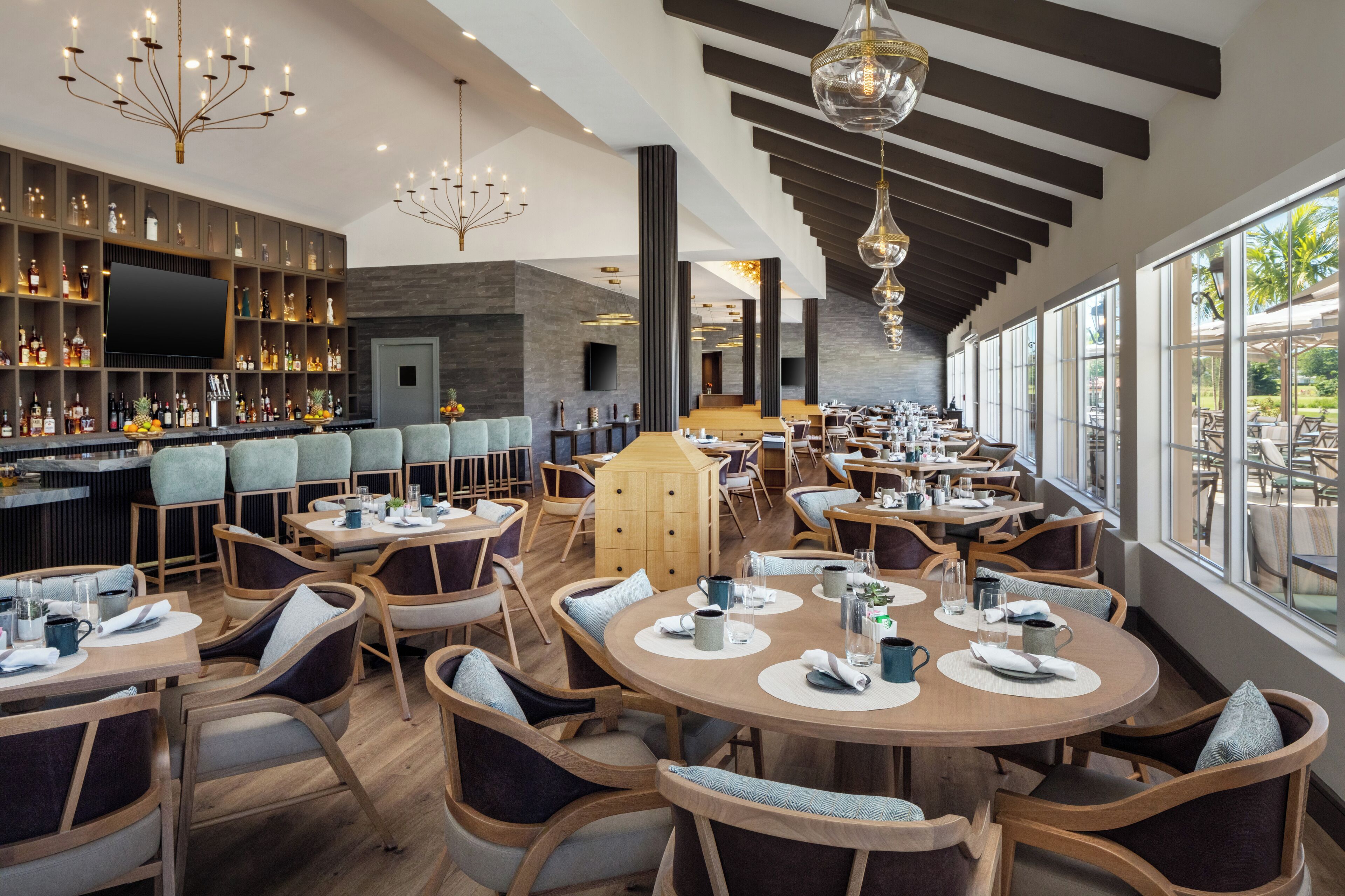 A modern restaurant with a bar area, round tables, and a view of the outdoors.