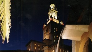 A nighttime view of a hotel with a large pool, a fountain, and a tower.