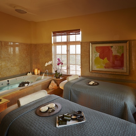 A spa room with two beds, a large bathtub, and a window with blinds.