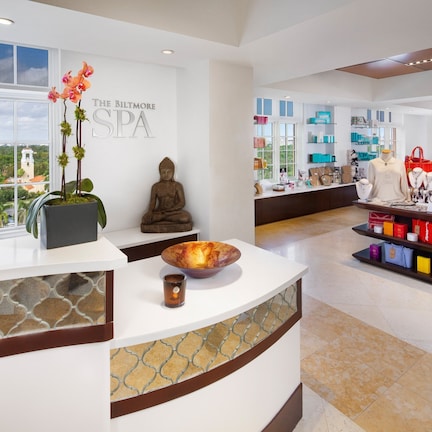 A spa reception area with a Buddha statue, a large window with a view of greenery, and a display of spa products.