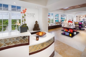 A spa reception area with a Buddha statue, a large window with a view of greenery, and a display of spa products.