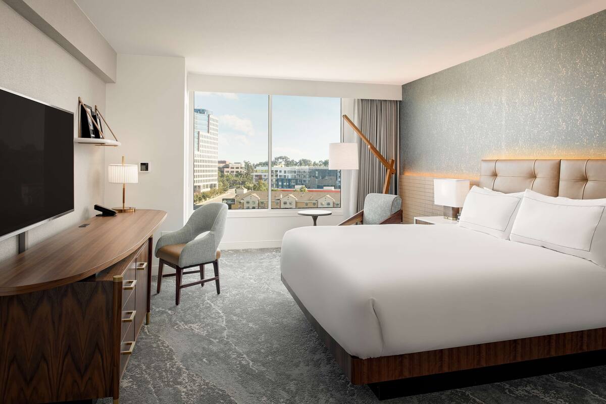 Une chambre d’hôtel dotée d’un grand lit, d’un bureau avec un téléviseur à écran plat, d’une chaise, d’une petite table et offrant une vue sur la ville grâce à de grandes fenêtres.