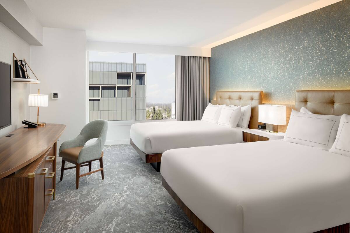 Une chambre d’hôtel avec deux lits, un bureau, une chaise et une grande fenêtre donnant sur la ville.