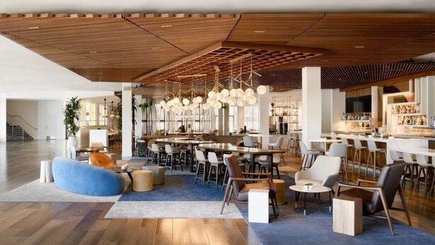 Een moderne bar met houten plafond, zitplaatsen en hangende lampen.
