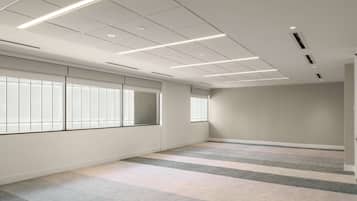 A spacious, well-lit room with large windows, a tiled floor, and a plain wall.